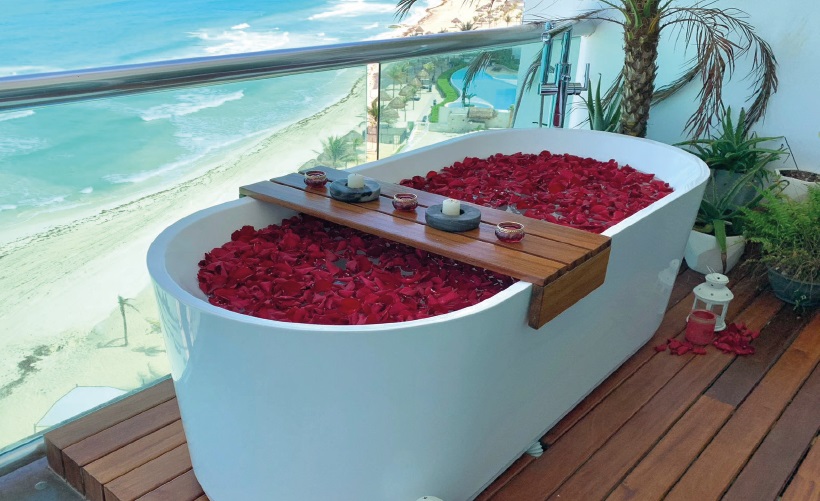 An intimate moment above the Caribbean — Villa Quarry Cancun features a private oceanfront bathtub surrounded by rose petals and endless sea views. | Un momento íntimo sobre el Caribe — Villa Quarry Cancún ofrece una bañera privada frente al mar con pétalos de rosa y vistas infinitas al océano.

