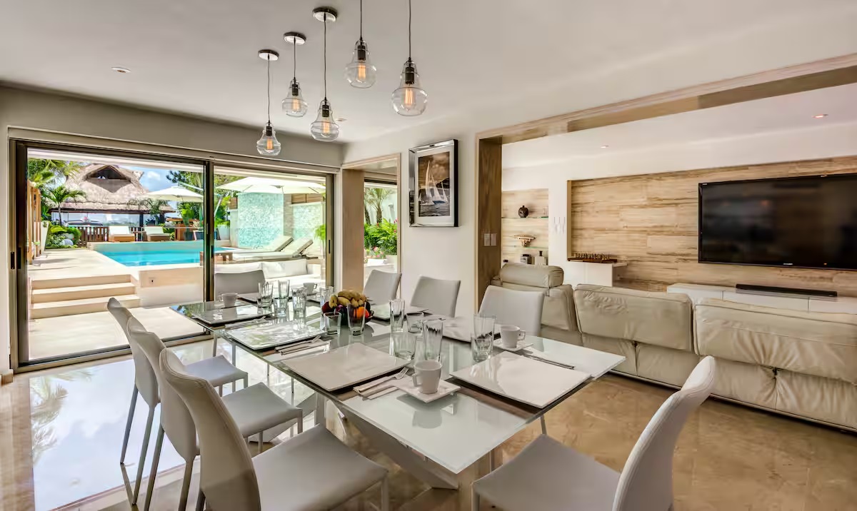 The open-concept living and dining area at Villa Patrón Cancun blends contemporary elegance with tropical charm, offering direct access to the pool and outdoor lounge. | El área de comedor y sala de Villa Patrón Cancún combina elegancia contemporánea con encanto tropical, ofreciendo acceso directo a la alberca y al lounge exterior.