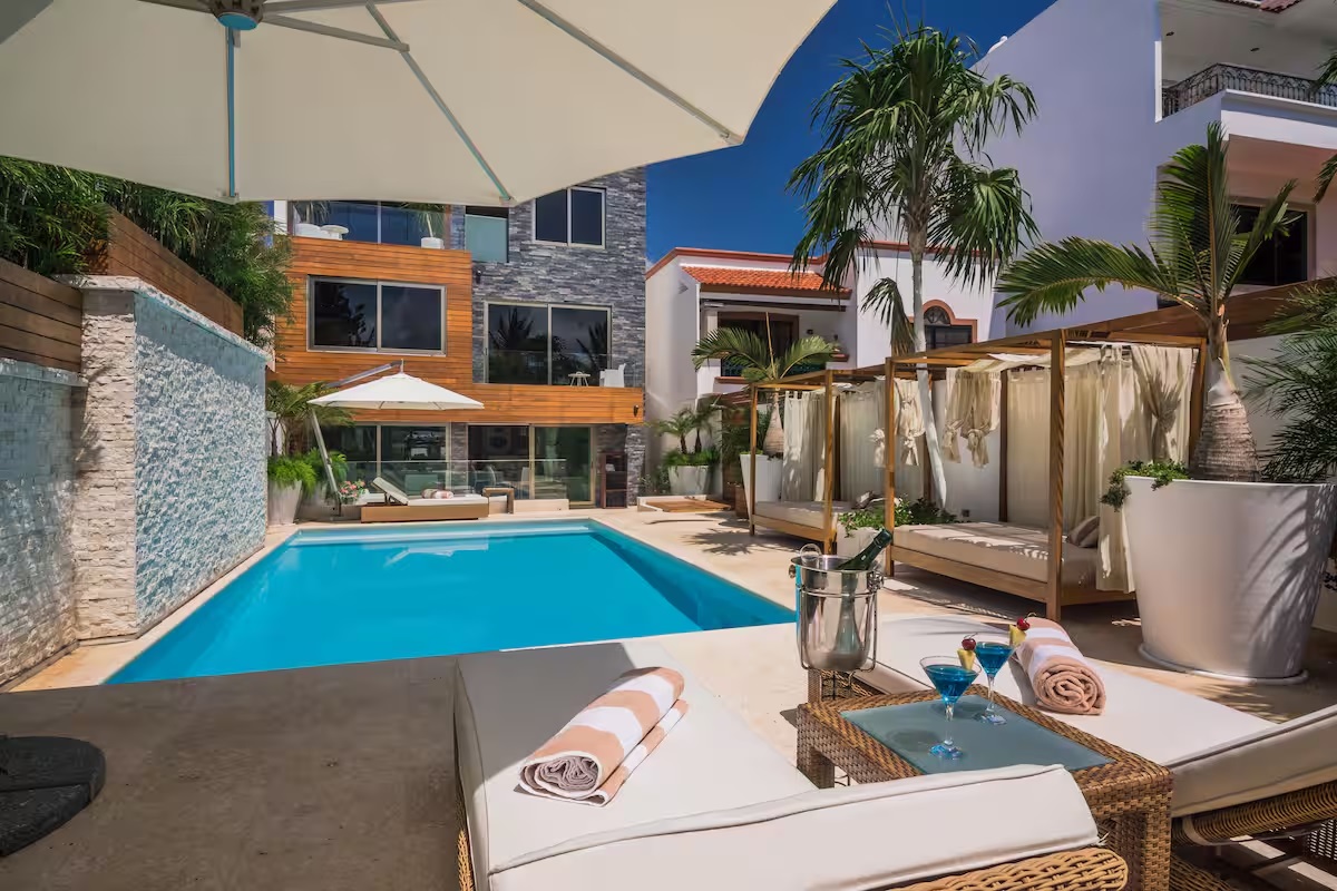 The main pool at Villa Patrón offers a resort-style atmosphere with cabanas, tropical palms, and elegant sun loungers — a private paradise in Cancun. | La alberca principal de Villa Patrón ofrece un ambiente tipo resort con camas balinesas, palmeras tropicales y elegantes camastros — un paraíso privado en Cancún.
