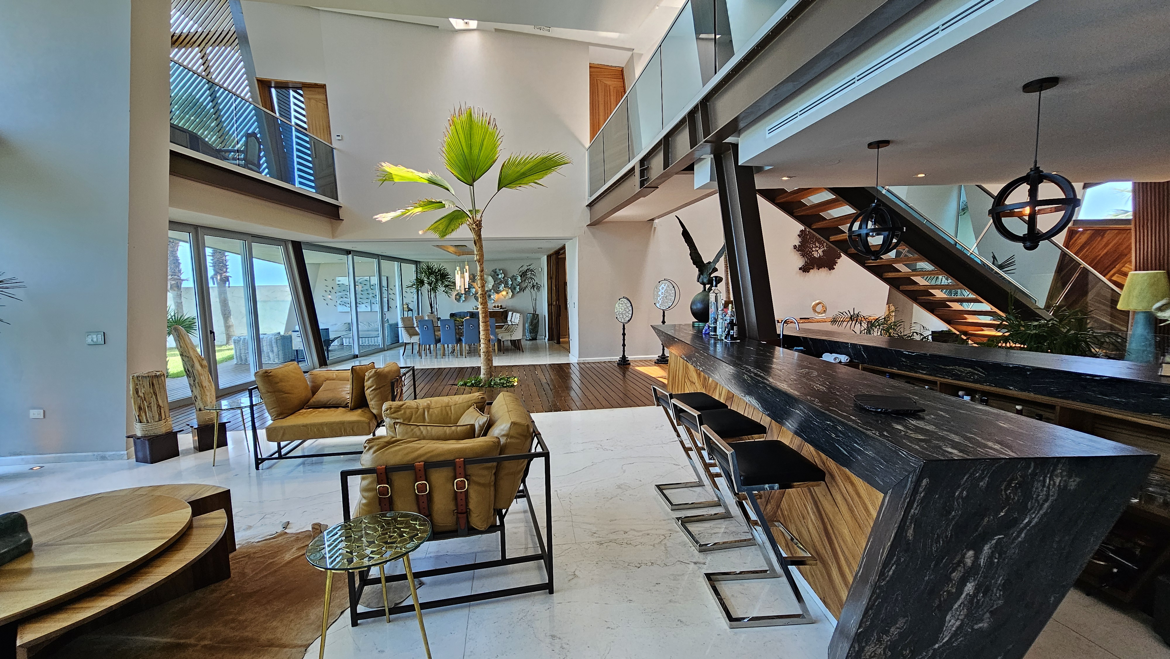 EN: Contemporary open-concept living area of a beachfront luxury villa in Cancun, featuring a sleek marble bar, modern staircase, indoor palm and panoramic ocean views. Designed for entertaining and relaxation, this elegant space combines natural materials with tropical elegance — part of I Live Where You Vacation’s Riviera Maya luxury villa collection.
ES: Área social de concepto abierto en una villa de lujo frente al mar en Cancún, con barra de mármol, escalera moderna, palma interior y vistas panorámicas al océano. Diseñada para el entretenimiento y la relajación, combina materiales naturales con elegancia tropical — parte de la colección de villas de lujo Riviera Maya de I Live Where You Vacation.
