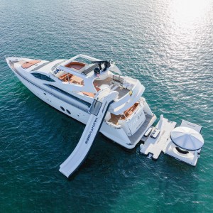 Aerial view of luxury yacht Truco VII 85 ft with inflatable slide and floating lounge in the Caribbean Sea – I Live Where You Vacation | Vista aérea del yate de lujo Truco VII de 85 pies con tobogán inflable y plataforma flotante en el mar Caribe – I Live Where You Vacation