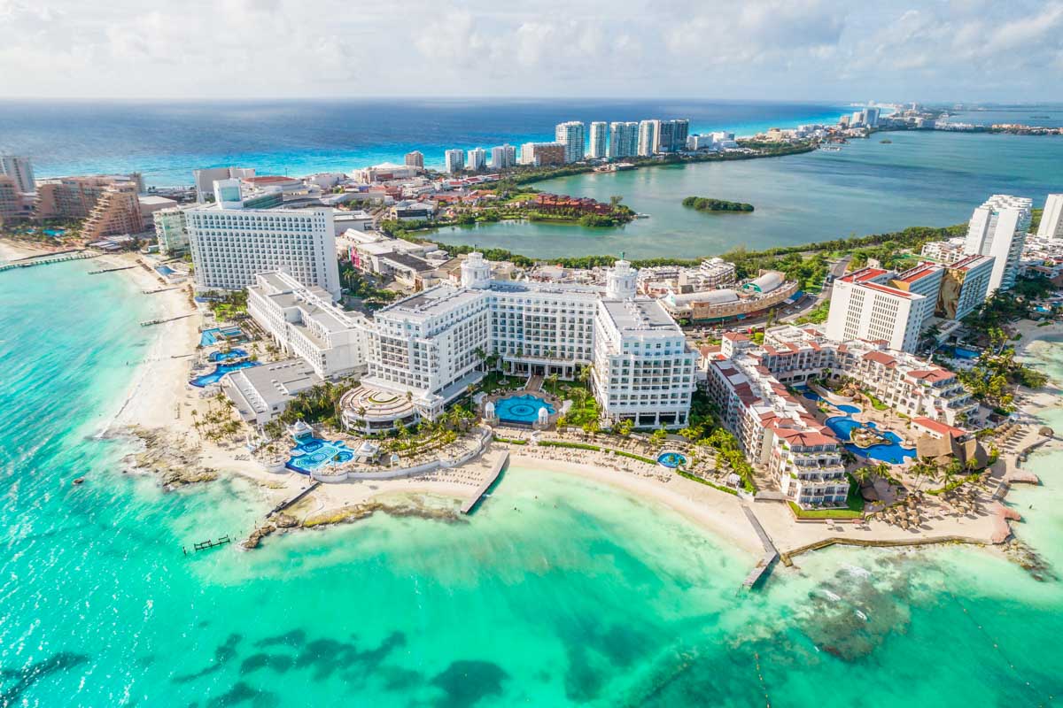 Aerial view of Cancún Hotel Zone with turquoise Caribbean Sea, white-sand beaches, and luxury resorts by I Live Where You Vacation. | Vista aérea de la Zona Hotelera de Cancún con el mar turquesa del Caribe, playas de arena blanca y resorts de lujo por I Live Where You Vacation.
