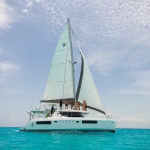 Fixer 45 ft catamaran sailing through turquoise waters in Cancún with guests on deck – I Live Where You Vacation | Catamarán Fixer 45 pies navegando por aguas turquesa en Cancún con invitados a bordo – I Live Where You Vacation