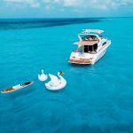 Sea Monkey 50 ft Sea Ray yacht aerial view with swan inflatables and paddleboard in turquoise Caribbean waters – I Live Where You Vacation | Vista aérea del yate Sea Monkey de 50 pies Sea Ray con inflables de cisne y paddleboard en aguas turquesa del Caribe – I Live Where You Vacation