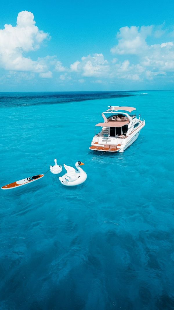 Sea Monkey 50 ft Sea Ray yacht aerial view with swan inflatables and paddleboard in turquoise Caribbean waters – I Live Where You Vacation | Vista aérea del yate Sea Monkey de 50 pies Sea Ray con inflables de cisne y paddleboard en aguas turquesa del Caribe – I Live Where You Vacation