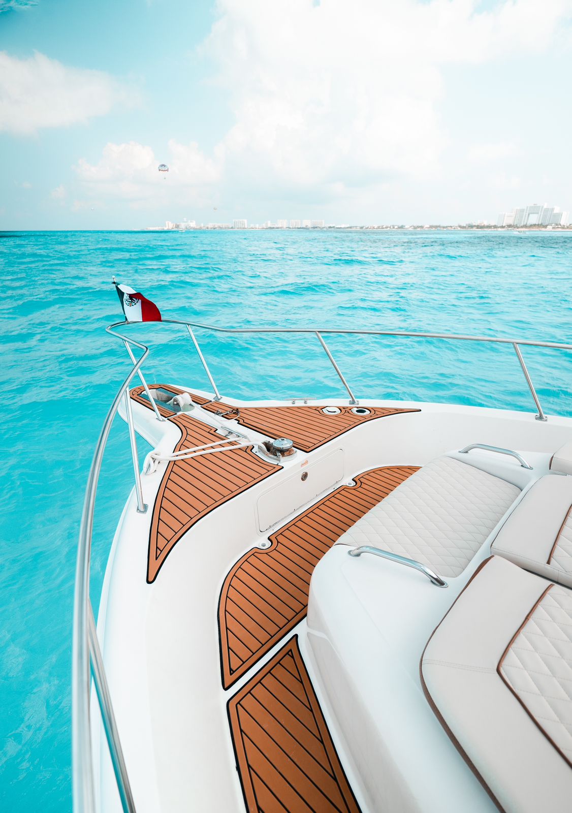 Elegant bow deck featuring teak-style flooring, quilted sun pads, and a proud Mexican flag overlooking the Caribbean. | Elegante proa con piso estilo teca, cojines acolchados y una orgullosa bandera mexicana sobre el Caribe.