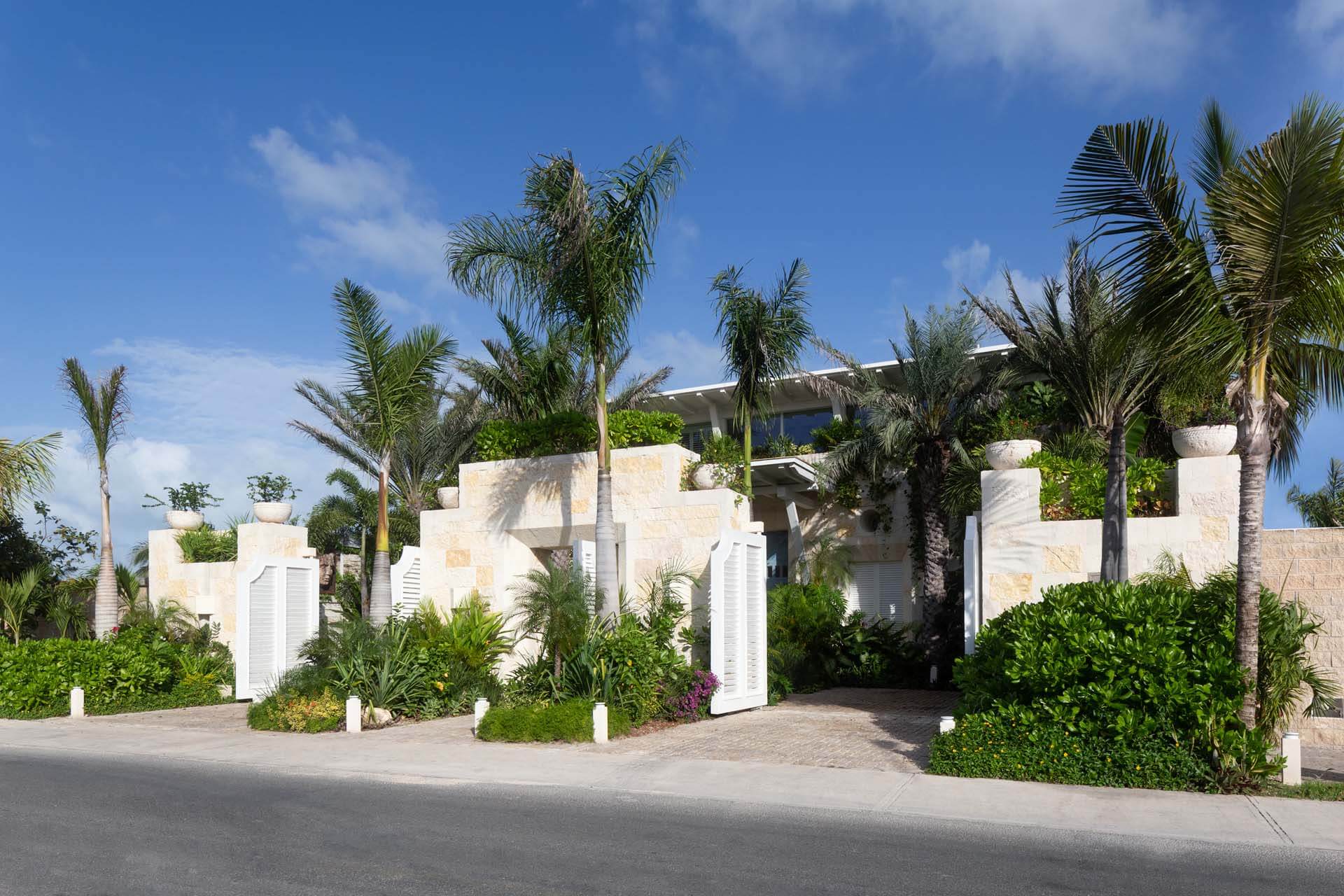 The sunlit entrance of Villa Sha in Cancun welcomes guests with palm-lined pathways, contemporary architecture, and tropical serenity — curated by I Live Where You Vacation. | La entrada bañada por el sol de Villa Sha en Cancún recibe a sus huéspedes con senderos rodeados de palmeras, arquitectura contemporánea y serenidad tropical — una experiencia curada por I Live Where You Vacation.
