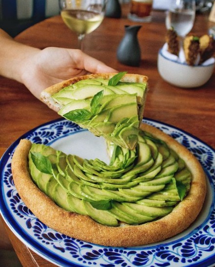 A handcrafted avocado pizza that blends freshness, artistry, and flavor, showcasing the elevated gastronomy of Tulum’s Riviera Maya scene. | Una pizza artesanal de aguacate que combina frescura, arte y sabor, reflejando la gastronomía elevada de la escena culinaria de Tulum en la Riviera Maya.
