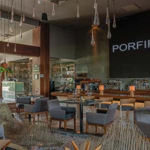 Elegant interior view of Porfirio’s Cancun restaurant, featuring modern design with warm wooden tones, artistic lighting, and a refined bar display of premium spirits – I Live Where You Vacation. | Vista interior elegante del restaurante Porfirio’s Cancún, con un diseño moderno de tonos cálidos en madera, iluminación artística y un refinado bar con licores premium – I Live Where You Vacation.