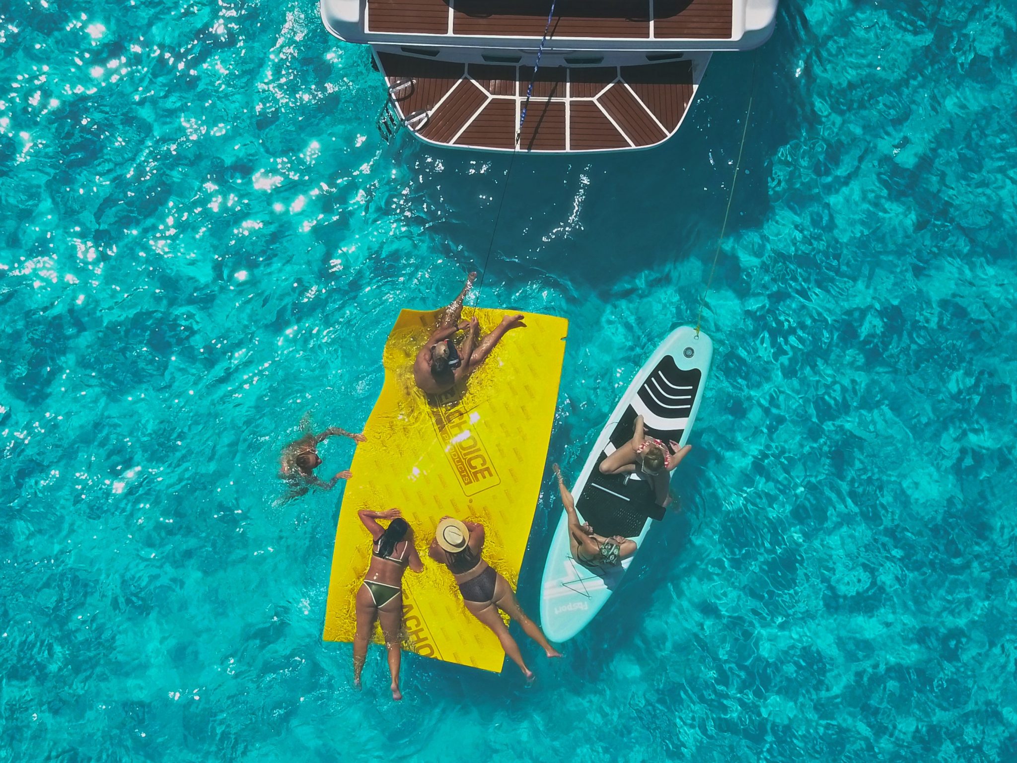 Guests enjoy the floating mat and paddleboard beside Jackie 46ft in turquoise Caribbean waters
